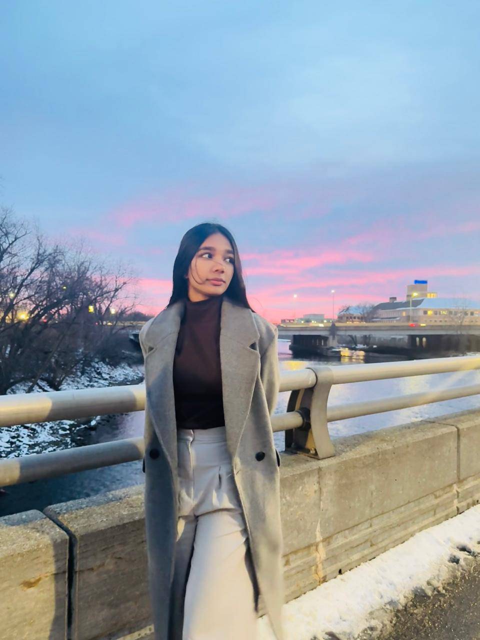Woman with black hair standing on a bridge with a sunset in the background